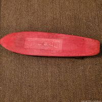 Photo of top side of the skateboard showing red plastic deck with 'CAL-240' embossed, placed on dark carpet.