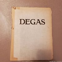 Front cover of the Degas book showing the title 'DEGAS' with visible wear and damage to the spine and edges of the cover.