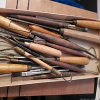 Photo showing a collection of vintage sculpting tools with wooden handles and various shaped metal working ends arranged in a tray