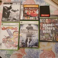 Photo showing the front covers of six games including Batman Arkham City (PS3), Art Academy (DS), Fairytale Fights (Xbox 360), Call of Duty World at War (Xbox 360), Grand Theft Auto IV (PS3), and a black Sub Hunt cartridge with red label.