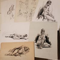 Layout of several nude figure sketches on white and beige paper showing seated, reclining, and standing poses with pencil and charcoal mediums