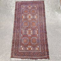 Full view of rectangular vintage Middle Eastern hand knotted rug on concrete showing overall pattern and colors.