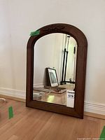 Full view of antique mirror with wood frame and curved top, showing placement against wall and reflection.