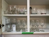 Shelf with assorted glassware; wine glasses, beer glasses, and shot glasses varying in size mostly clear glass