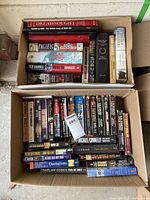 Two boxes of assorted used hardcover and paperback books, visible titles include 'Dreadnought', 'Pacific', 'Rush to Danger', 'The End of War', 'American Caesar', and several thriller novels.