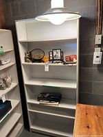 Front view of white bookshelf showing shelves and some items temporarily placed. The shelves are empty apart from some items not included in the lot.