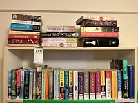 Wide view of bookshelf packed with various hardcover and paperback books by different authors including Nora Roberts, Daniel Silva, J.K. Rowling