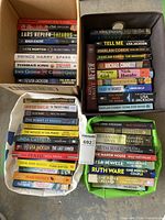 Multiple containers (cardboard box, fabric bags) filled with books by bestselling authors in fiction and non-fiction genres.
