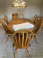 Full set view showing oval dining table with six matching spindle-back chairs and table pad on top