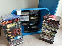 Blue storage bin with stacked DVDs, showing multiple DVD titles and series stored inside and beside it.