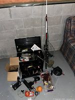 Open black plastic tackle box with tools and papers, two rods and net leaning.