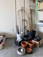 Photo of assorted garden stakes, bamboo poles, plastic and clay planters in a corner.