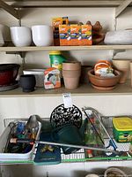 Shelves with mixed gardening items including planters, insect repellent boxes, Miracle-Gro container, and assorted gardening tools on a wire shelf below