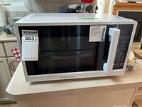 Front view of the white Insignia microwave with control panel and handle visible, placed on a kitchen countertop.