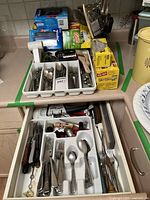 Countertop and partly open drawer showing cutlery trays with forks, spoons, knives, and boxes of plastic wrap and resealable plastic bags.