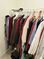 View of hanging clothing on a white wire rack showing varied colors and styles including knit sweaters and jackets.