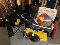 Overall lot of camping and outdoor gear including cooler, chair, bags, kite, and accessories laid out on floor