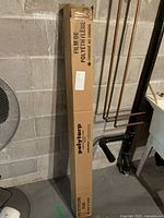 Full cardboard box packaging of Polytarp polyethylene film standing upright against a concrete wall.