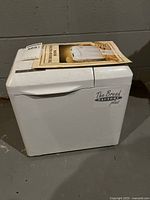 Full view of white bread maker with manual on top showing overall condition.