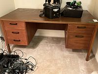 Front view of a medium brown wooden desk with six drawers showing the whole desk structure and some of the items on top and around it.