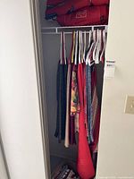 Closet with multiple hanging textiles including blankets and linens, some in red and dark tones