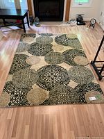 Full view of the rug laid flat on hardwood floor beneath a fireplace, showing overall pattern and condition.