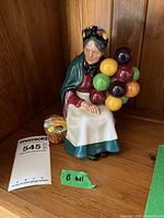 Front view of Royal Doulton figurine showing elderly woman holding colorful balloons with basket nearby.