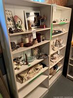 Photo of two white wooden bookcase shelves placed side by side filled with miscellaneous decorative items and some wear marks visible on the shelves.