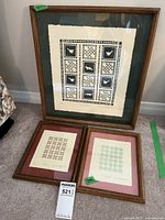 Three framed artworks arranged on carpet, showing all pieces together including the large main piece and two smaller pieces beneath.