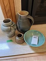 Four unique handcrafted ceramic items: large pitcher, two vases, turquoise bowl, displayed together on countertop.