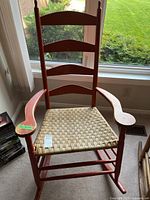 Front view of the wood and wicker rocking chair showing the woven seat, curved armrests, and backrest slats.