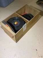 Wooden box with two compartments filled with vintage 45 RPM records without sleeves.
