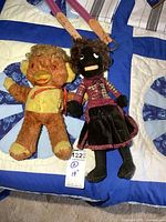 Photo of two antique dolls lying on a quilt, one plush brown with yellow face and orange beak, the other with dark complexion and curly hair wearing magenta jacket and black skirt.