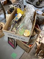 Two cardboard boxes on the floor filled with various vintage bottle openers, local buttons in a plastic bag, and a Playboy calendar.