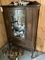 Oblique angled view of the same vintage wooden china cabinet showing detail of legs and drawer handles, along with a few unrelated items on the floor.