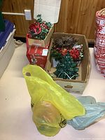 Overview photo showing cardboard boxes containing multiple Christmas decorations including wreaths, artificial flowers, and wrapped items, taken to show the full lot contents.