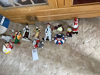 Collection laid out on carpet in front of wooden cabinet, showing all 11 vintage porcelain clown figures in various poses and colors.