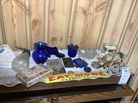 Display of various vintage collectibles including wind-up donkey, blue glass items, small booklets, metal and ceramic pieces, and an Eatmore Peanut Chew sign on a shelf.