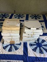 Stack of twelve boxed plates shown in original packaging on a quilted bedspread.