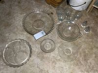 Full view of glass items including two large serving dishes with beaded rims and etched floral Cornflower pattern, divided plate, small bowl, five drinking glasses and salt and pepper shakers.