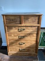 Front view showing all five drawers, carved floral details on top two drawers, one missing knob, and brass handles on bottom three drawers.