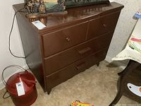 Photo showing full view of brown painted wood dresser with three drawers on short legs.