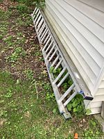 Full length rear angle view of the aluminum extension ladder resting on the ground near a house, showing condition and overall length.