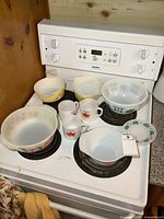 Overview of mixing bowls, mugs, casserole dishes on stove top showing wear and pattern details