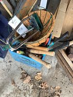 Overview photo of the milk crate contents showing garden hand tools, green metal hanging basket with coir liner, and part of lawn sprinkler and watering can.