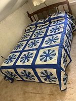 Dark blue quilt with floral patterned squares spread over a wooden bed, shows minor wear and fabric texture