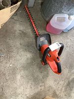Full view of Black & Decker electric hedge trimmer placed on concrete floor near some containers.