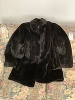 Front view of ladies London Fog faux fur coat, black with a high collar and button closure, laid flat on floral patterned surface.