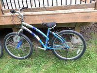 Full side view of the blue, silver, and purple Kent Sierra Madre mountain bike leaning against a wooden deck with 26 inch tires and a kickstand.