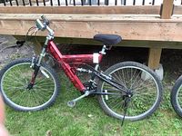 Full side view of the black canyon mountain bike leaning against a wooden deck, showing red aluminum frame and kickstand.